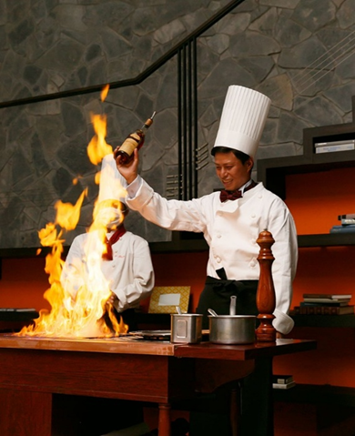 【名古屋市結婚式場ビアンカーラテラス】披露宴のメインディッシュを彩る大迫力のフランベ演出。名古屋市の中心部に位置する市内の会場で、シェフや新郎がゲストの目の前で高く上がる炎を上げ、お肉料理を一気に香りづけして仕上げるドラマティックな瞬間を描写した、最高に盛り上がるおもてなしの演出です。
