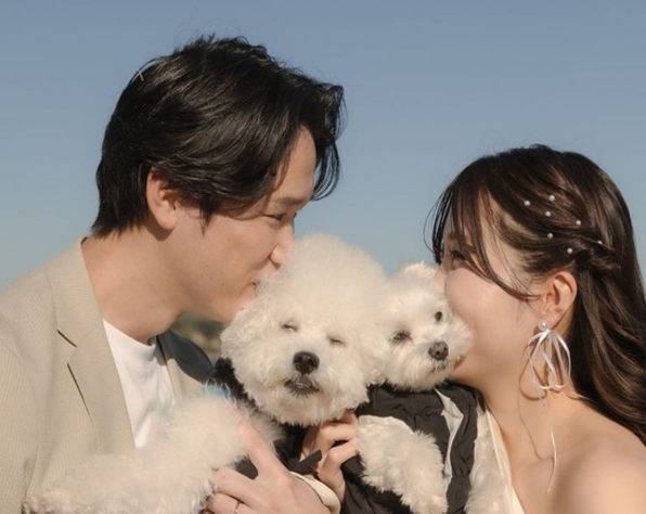 名古屋市結婚式場ビアンカーラヒルサイドテラス。愛犬の白いプードル2匹を抱きかかえ、幸せそうに寄り添う新郎新婦。澄み渡る青空の下で、家族の一員であるペットと共に叶えるアットホームなウェディングフォト。