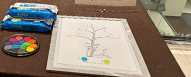 ブラウンのテーブルに、ウェディングツリーのイラスト台紙とカラフルなスタンプパレット、ゲスト用のおしぼりが並べられた結婚式の演出コーナー。