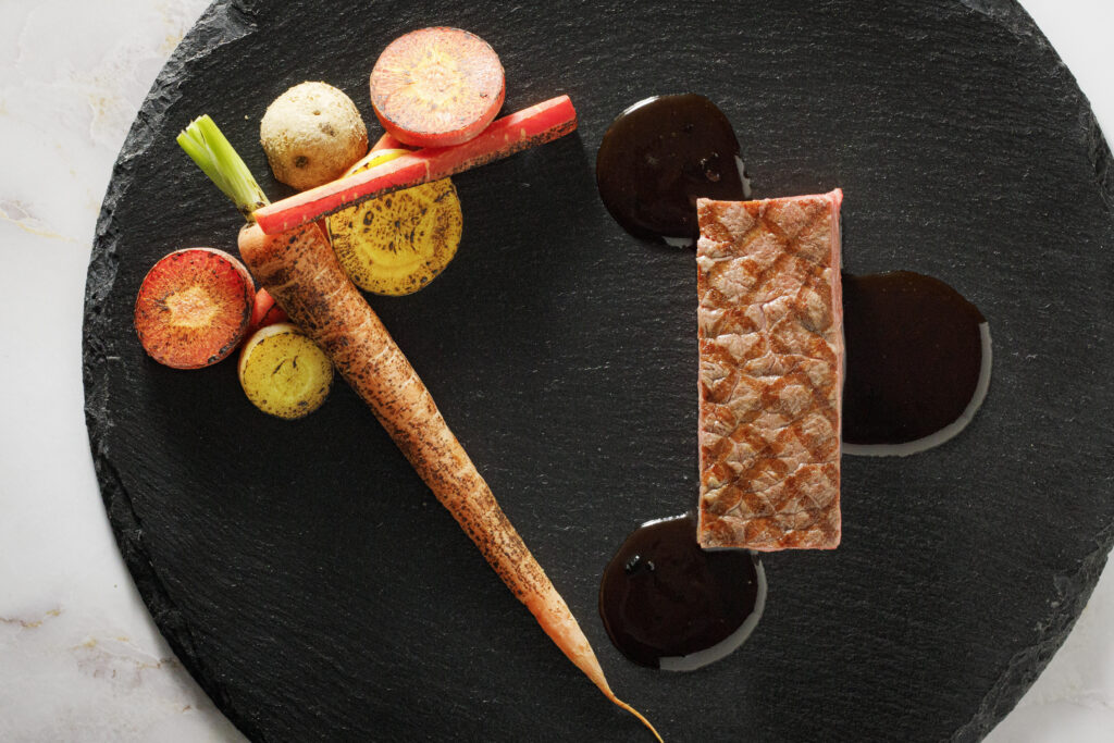 名古屋市の結婚式場ビアンカーラヒルサイドテラスの婚礼料理。厳選された牛フィレ肉のグリルと色鮮やかな旬の根菜が、黒いスレート皿に美しく映える逸品です。