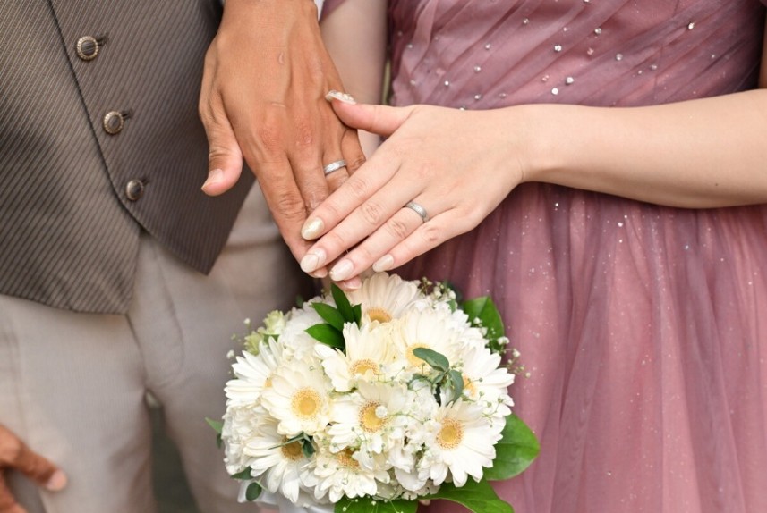 名古屋市の結婚式場ビアンカーラヒルサイドテラスで撮影された、赤いバラのブーケに手を重ねる新郎新婦。左手薬指に輝く結婚指輪をクローズアップした幸せの一枚。