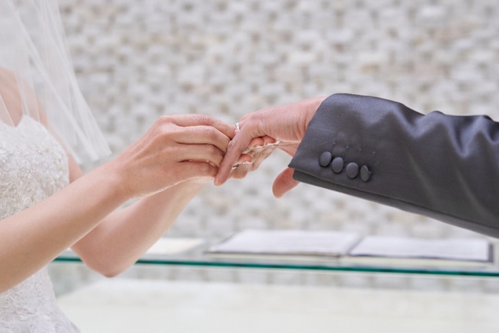 名古屋市の結婚式場ビアンカーラヒルサイドテラスでの挙式。光溢れるチャペルで、花嫁が新郎の指に結婚指輪をはめる感動的な指輪交換の瞬間。