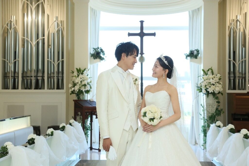 名古屋市の結婚式場ビアンカーラヒルサイドテラス。柔らかな自然光に包まれた純白のチャペルで、見つめ合う新郎新婦。洗練されたアーバンリゾート挙式の誓い。